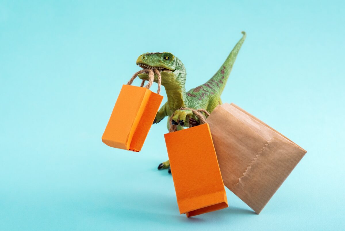 Cute green dinosaur with shopping bags on a blue background. Cute humor shopping concept.