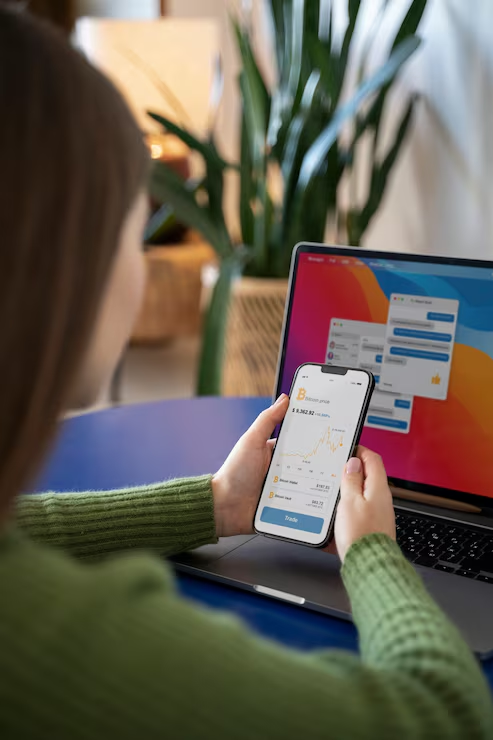 Woman checking bitcoin price on phone near laptop, web design in Myrtle Beach